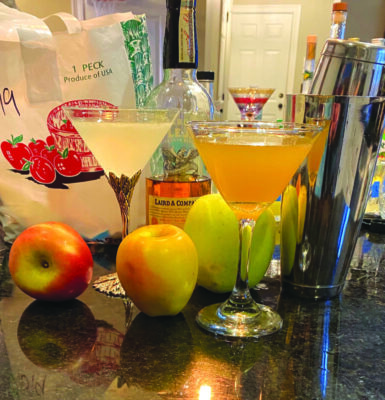 2 cocktails in martini glasses on counter surrounded by apples