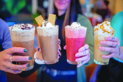women holding 4 flavors of shakes with whipped cream on top