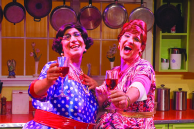 2 drag performers dressed in character toasting with wine glasses in kitchen