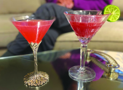 2 cocktails in martini glasses, one with lime wheel, on shiny coffee table