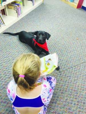 young girl sitting on floor reading book to therapy dog