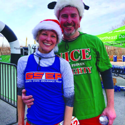 a man and a woman wearing santa hats, dressed for race on a cold day