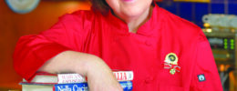 woman in red chef jacket posing with on arm on a pile of cookbooks