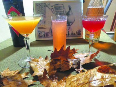 3 drinks in cocktail glasses on table with leaves