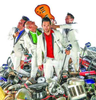 4 band members standing in pile of metal wearing shiny suits