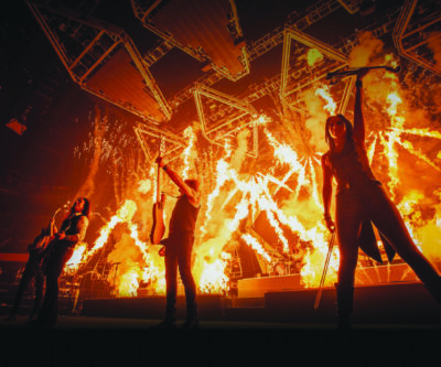 musicians on stage lit up by fiery background effects, holding up the instruments