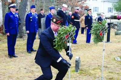 military personnel in dress uniform standing at attention in cemetery, one man placing wreath on stand