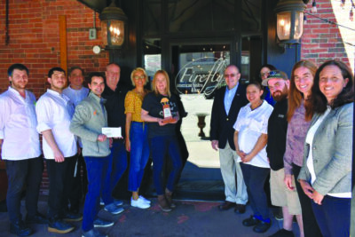 group of people standing outside door with restaurant name on it, woman in center holding trophy