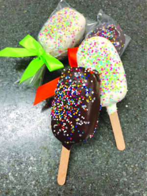 cake covered in chocolate and decorated with sprinkles on a popsicle stick