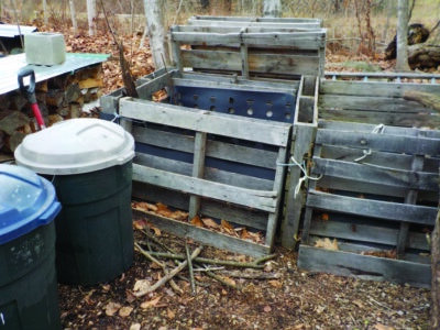 wooden, slatted compost bins, plastic barrels sitting beside them