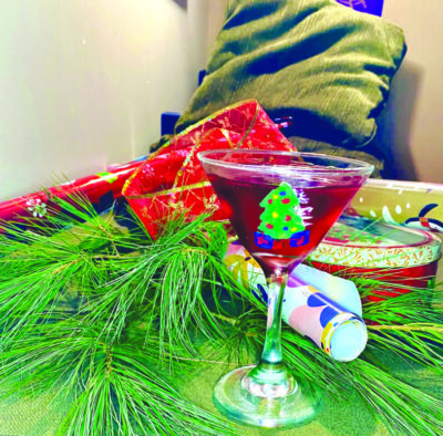 martini glass painted with colored chocolate sitting on table with pine boughs, wrapping paper and ribbon