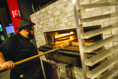 man pulling pizzas out of brick oven