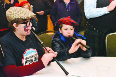 a young girl and an older boy sitting at round table and playing Scottish pipes