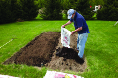 man pouring compost onto dug out section of lawn