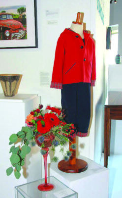 artwork in gallery space, fiber art coat and pants with flower arrangement beside it