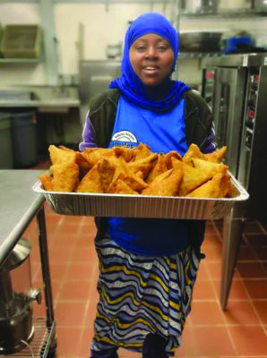 Somali woman wearing headscarf, holding tray of meat pies