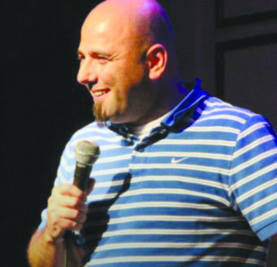 man in striped shirt, balding and with beard, laughing holding microphone