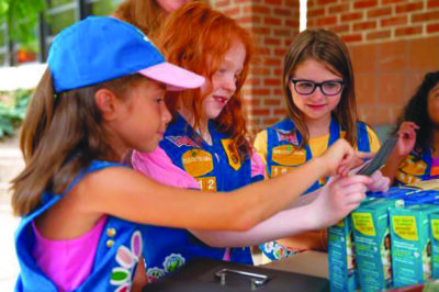 3 young girl scouts arranging cookies boxes on table