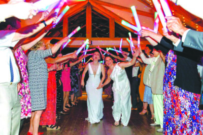 2 brides walking rows of celebrating guests at indoor venue