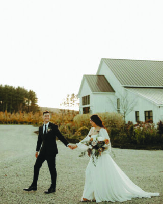 groom and bride walking hand in hand outdoors in front of white building