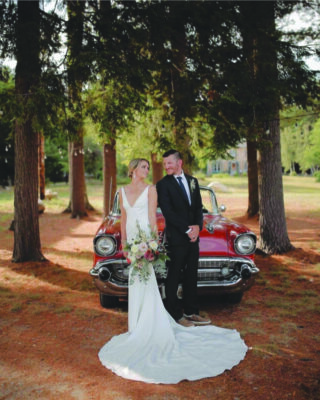 bride and groom outside standing in front of red vintage car surrounded by trees