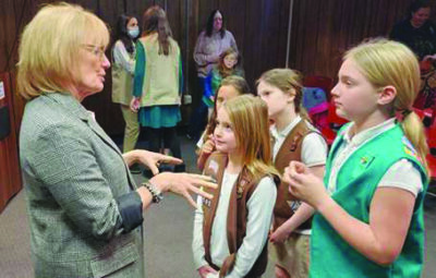 woman in business suit talking with young girl scouts