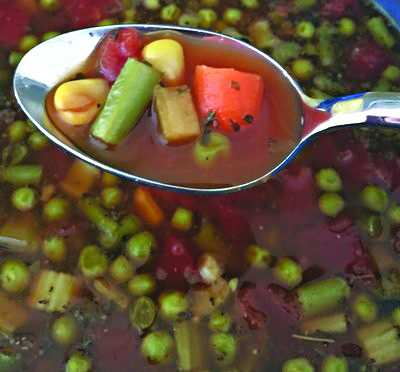 spoon holding vegetable soup raised over vegetable soup