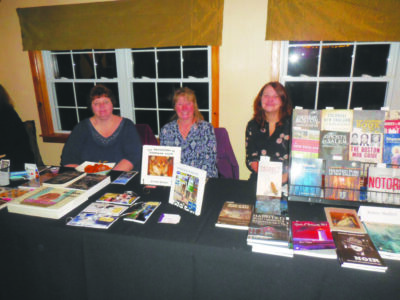 3 women sitting behind display tables covered with books at author's event