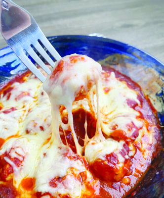 fork digging into bowl of meatballs covered in cheese and sauce