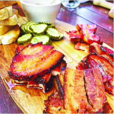 wooden restaurant platter loaded with bacon, pickles and dipping sauce