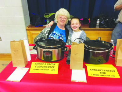 older woman and girl sitting at table, with crockpots of chili