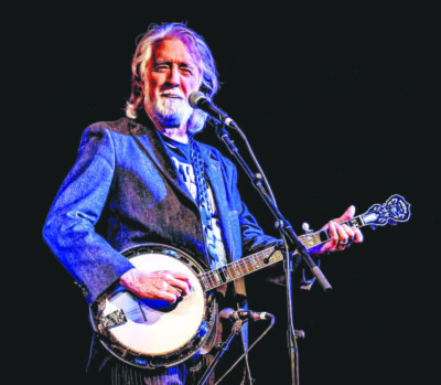 man with white beard and long hair standing in front of standing microphone while playing banjo
