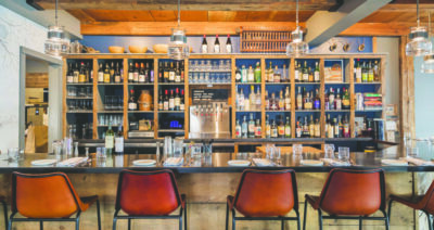 chairs lines up against bar, facing shelves of alcohol, sleek wooden style