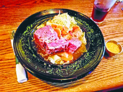 plate of corned beef and cabbage beside drink glass on wooden table