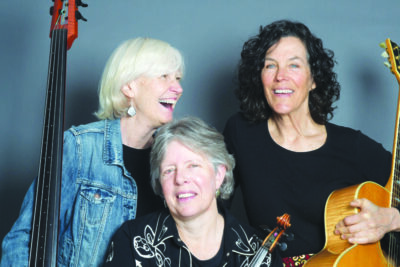 three mature women holding string instruments and laughing together