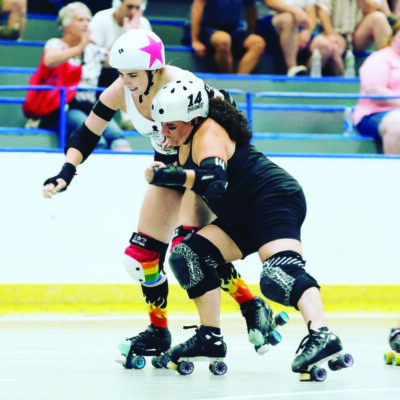 one women on roller skates and protective gear slamming into another woman on roller skates and protective gear during roller derby