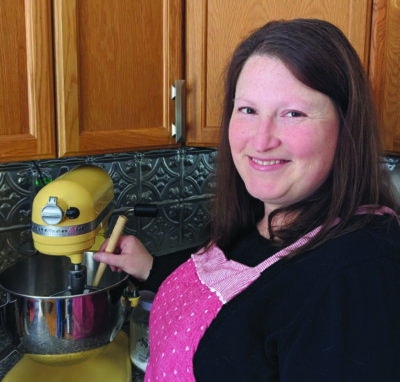 woman wearing apron, standing in kitchen beside electric mixer