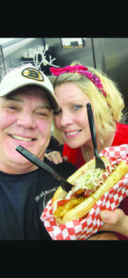 man and woman holding up meat sub with 2 forks stuck in it