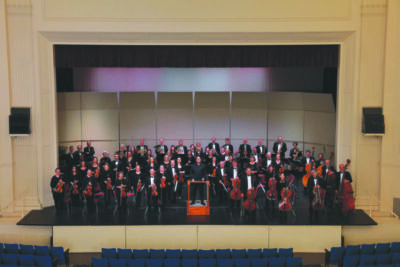 Full orchestra standing on stage with instruments