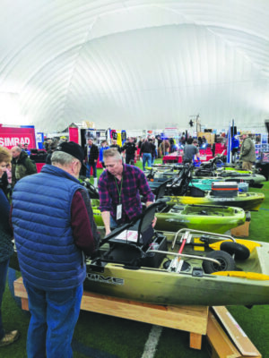 2 men looking at dispaly of duck hunting boats in big tent at outdoor expo