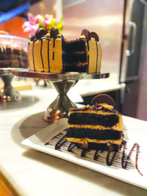 chocolate cake decorated with reese's peanut butter cups, on cakestand on restaurant counter, plate with one piece of cut cake