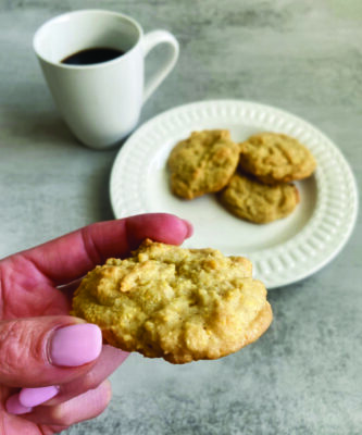 3 cookies on a plate near mug of coffee, hand holding 1 cookie above plate