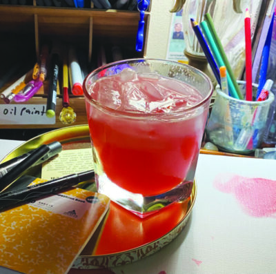 red cocktail in short glass sitting on desk with pencils