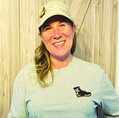 woman wearing baseball cap with hair in pony tail standing in front of wooden wall, smiling