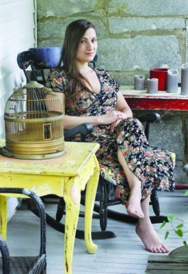 young woman wearing long dress with no shoes, sitting in rocking chair on porch