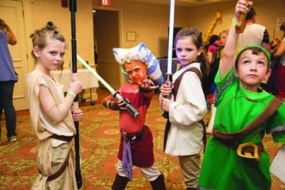 4 kids dressed as star wars and zelda characters, posing together in room at event