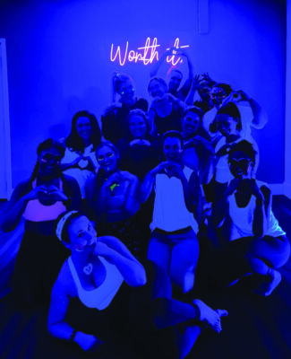 group of women in exercise gear, posing in group under dark blue light