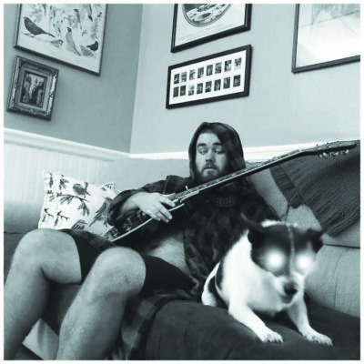 man with guitar sitting on couch with medium sized dog