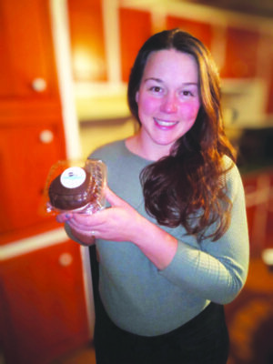 woman holding up wrapped baked good, smiling, standing in kitchen, blurred background