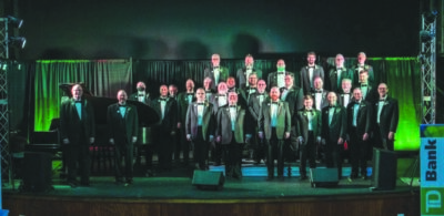 large group of men in tuxedos standing on stage under green and blue light